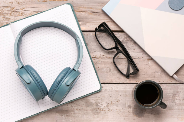 Modern blue headphones with notebook and eyeglasses on grey wooden background - Foto, Bild
