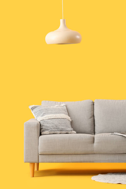 Acogedor sofá gris con cojín sobre fondo amarillo - Foto, imagen