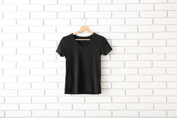 Black t-shirt hanging on white brick wall - Foto, imagen