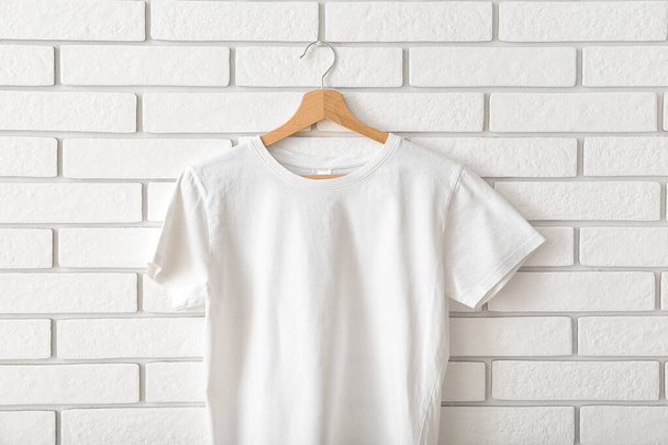 Stylish t-shirt hanging on white brick wall - Fotó, kép