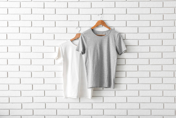 Stylish t-shirts hanging on white brick wall - Photo, image