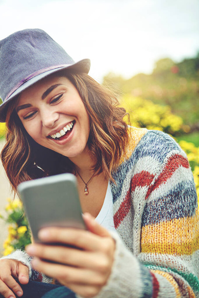 Condividere la sua giornata all'aria aperta con i suoi amici online. una giovane donna attraente che utilizza un telefono cellulare durante una giornata primaverile all'aperto - Foto, immagini