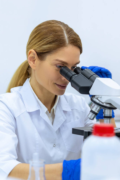 Medical female scientist looking under microscope, doing analysis of test sample, ambitious biotechnology specialist working in laboratory. - Fotó, kép