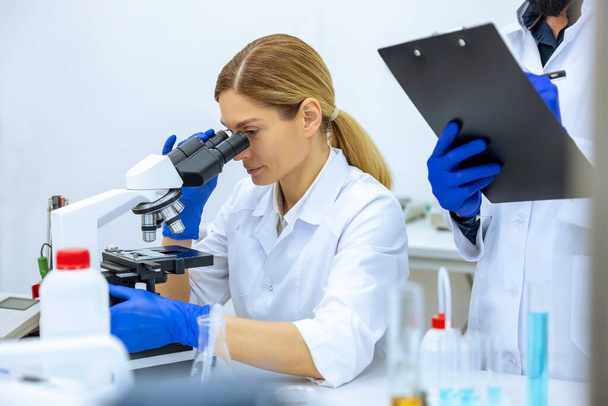 Woman and man scientists in lab coat making notes after doing sample test in laboratory, professional worker analyzes received data together. - Фото, изображение