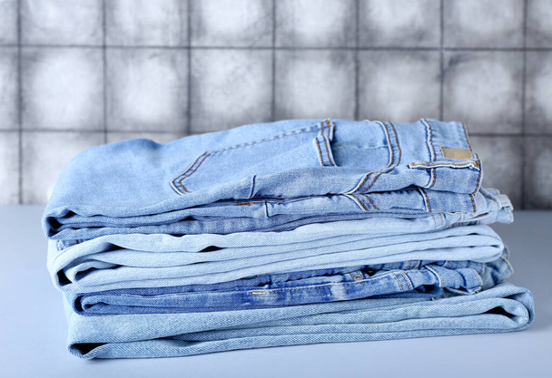 Pila di jeans sul tavolo vicino parete piastrelle grigie - Foto, immagini