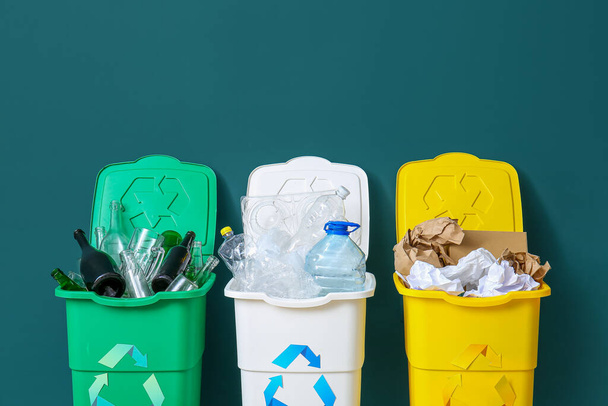 Κάδοι απορριμμάτων με σύμβολο ανακύκλωσης και διάφορα σκουπίδια κοντά σε πράσινο τοίχο - Φωτογραφία, εικόνα