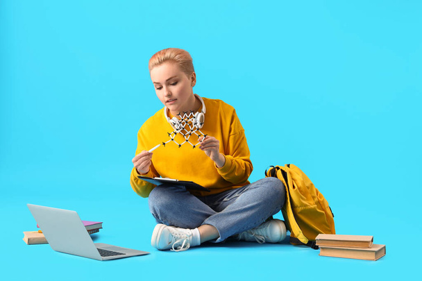 Female student studying with molecular model on blue background - Foto, Imagem