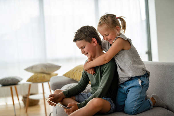 Little girl and boy watching video or playing games on their digital device tablet, smartphone. Children digital addiction concept. - Photo, image