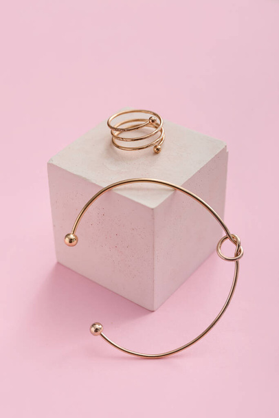 Pedestal de escaparate con anillo de oro y pulsera sobre fondo rosa - Foto, imagen