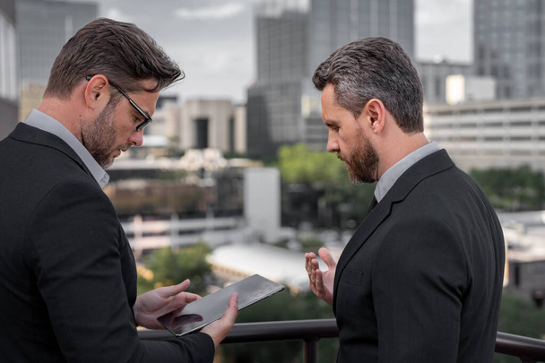 Photo of business partners talk conversation outdoor. Two handsome businessmen in suits discuss a working project against the background of urban city. Cooperation concept - Foto, Bild