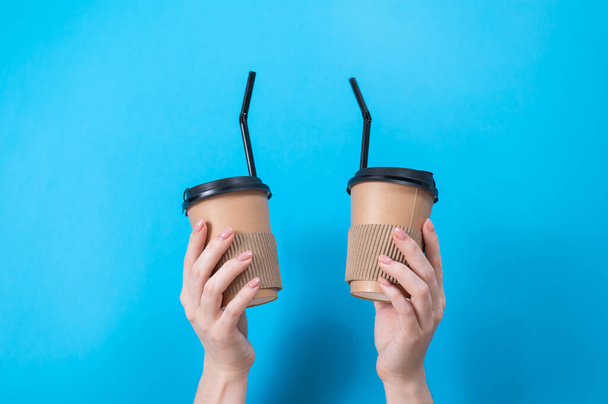 A woman holds two cardboard cups with coffee on a blue background - Foto, immagini