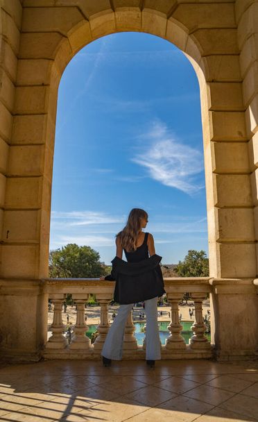 Silueta retroiluminada de la hermosa joven modelo de moda con el pelo largo y rubio en jeans azules, gafas de sol, top negro y jeans azules de pie bajo un arco de piedra del monumento al parque Ciudadela de Barcelona - Foto, imagen