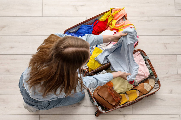 Молода жінка роздягається з валізи на світлій дерев'яній підлозі
 - Фото, зображення