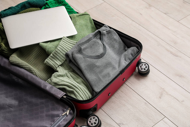 Open suitcase with laptop and sweaters on light wooden floor - Foto, Bild