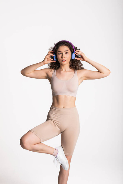 Fit and healthy sport girl, female athlete dancing and listening music in wireless headphones, laughing and smiling, wearing activewear, white background. - Foto, immagini