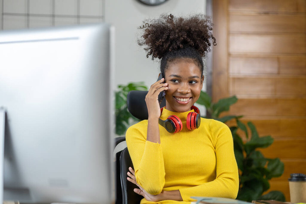 Молодая американка - начинающая предпринимательница, сидит в своем офисе и говорит по телефону со своим партнером, менеджментом и бизнесом из нового поколения. Концепция управления стартапом. - Фото, изображение