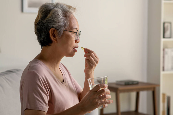 Asiatische Seniorin, die Medizin zu Hause einnimmt, Alter, Medizin, Gesundheitswesen und Menschen-Konzept - Foto, Bild