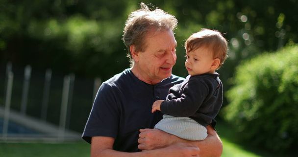 Grand-father holding baby infant in arms outside in backyard. Grand parent bonding with grand-child - Fotoğraf, Görsel