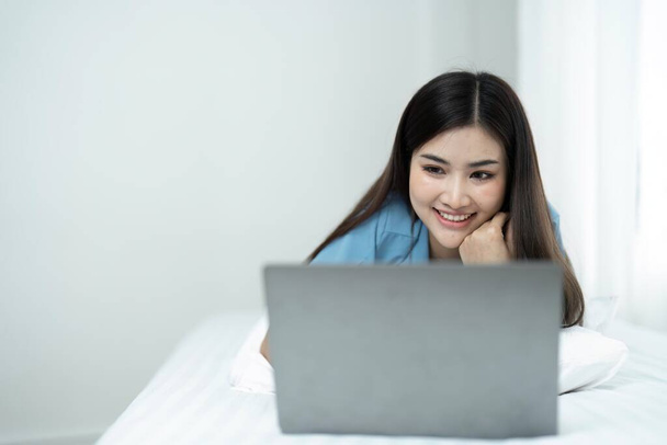Kaunis nuori nainen rentouttava sängyllä käyttää kannettavaa tietokonetta pelata sosiaalista mediaa kotona. - Valokuva, kuva