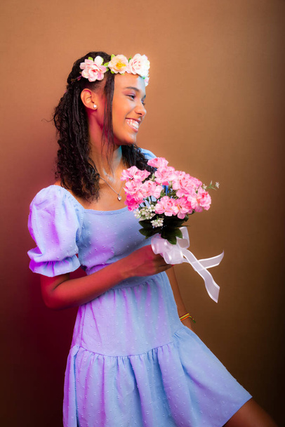 Portrait of beautiful girl, teenager, wearing blue, with tiara on her head and holding bouquet of flowers. Isolated on brown background. - Foto, imagen