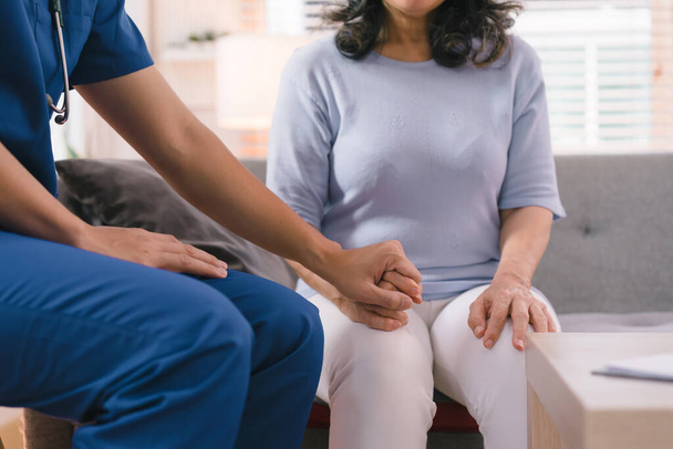 A young caregiver is consulting with a 60-year-old Asian elderly woman, providing encouragement and taking a medical history. The two are shown holding hands and exchanging words of encouragement - Photo, image