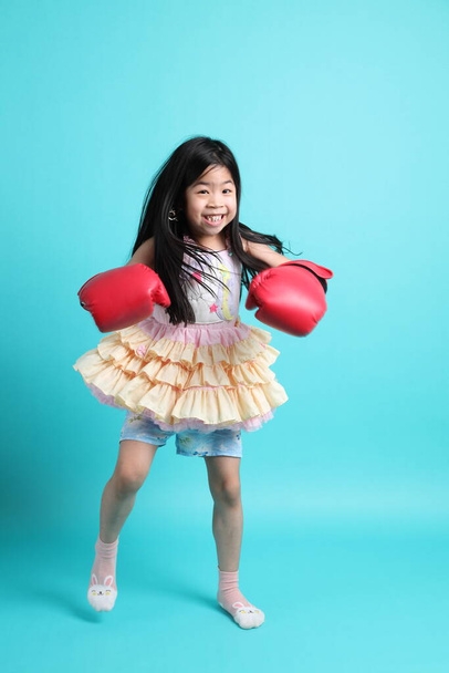 Das süße asiatische Mädchen mit Boxhandschuhen steht auf dem grünen Hintergrund. - Foto, Bild
