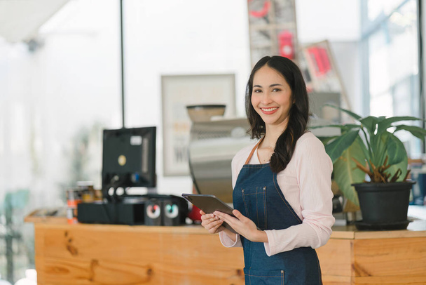 Portrait of confident female barista standing at counter. Woman cafe owner in apron looking at camera and smiling while welcoming guests - Photo, Image