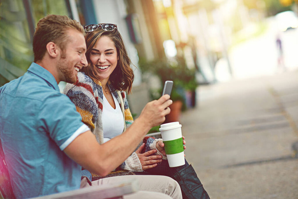 Devrions-nous poster notre selfie en ligne. un jeune couple heureux utilisant un smartphone ensemble tout en passant la journée au centre-ville - Photo, image