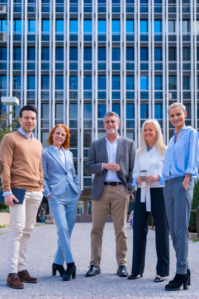 Portrait of cheerful group of coworkers walking outdoors in a corporate office area, with an office building in the background - Foto, Imagem