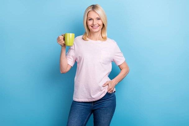 Portrait of friendly optimistic senior woman with bob hairstyle wear white t-shirt hold mug of coffee isolated on blue color background. - Φωτογραφία, εικόνα