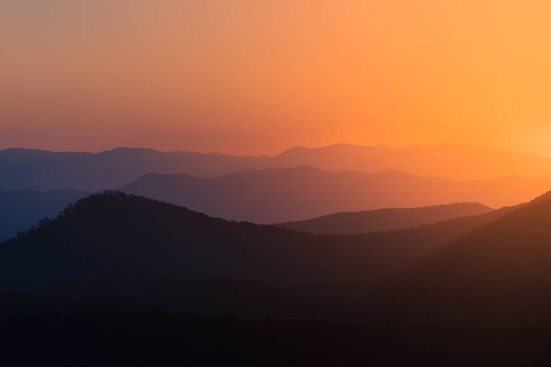 A silhouette view of the peaks of mountain range under colorful dusk sky at sunset - Fotó, kép