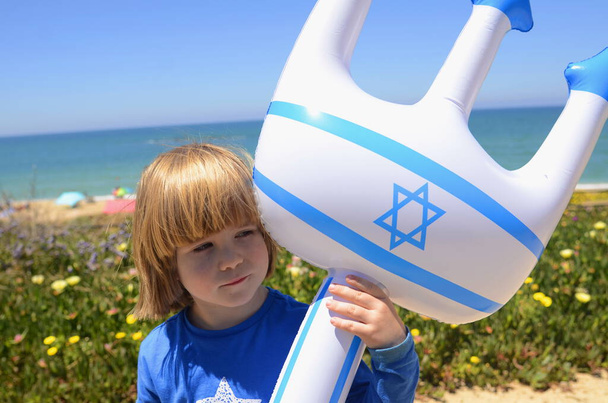 Egy kisfiú felfújható játékkal az izraeli zászlóval és Dávid Csillagával. Koncepció: izraeli üdülőhelyek, strandok, tenger. Izrael Függetlenség Napja, hazafiság. - Fotó, kép