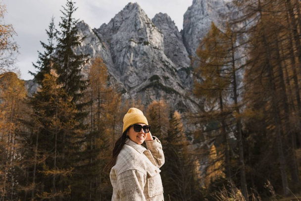 Smiling young woman standing in front of larch trees under beautiful mountains in autumn - Zdjęcie, obraz