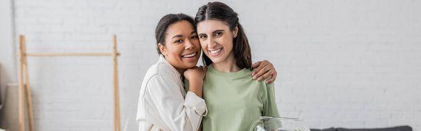 overjoyed multiracial woman hugging lesbian partner in new house, banner  - Photo, Image