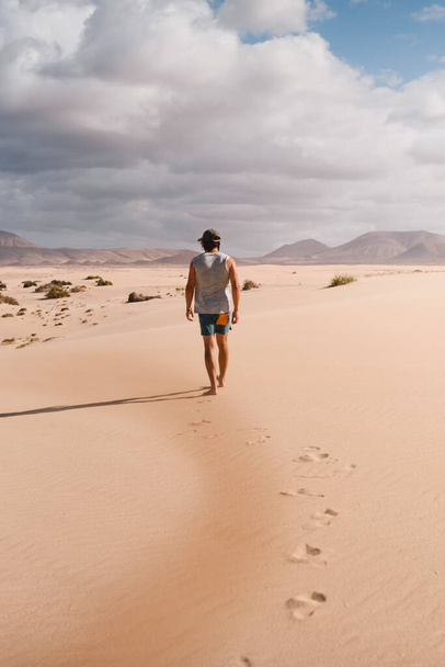 Young man walking calmly on the desert sand of the dunes of Corralejo in Fuerteventura, in summer, during a vacation trip through the Canary Islands - Photo, Image