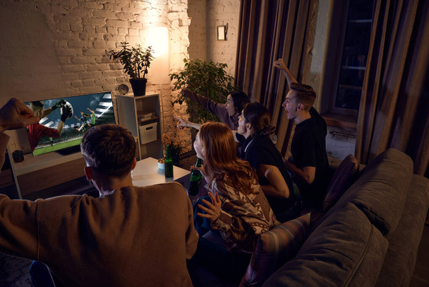 Group of friends watching live american football translation, cheering up team and drinking beer at home in evening. Concept of friendship, leisure activity, weekends, fun, emotions - Fotografie, Obrázek