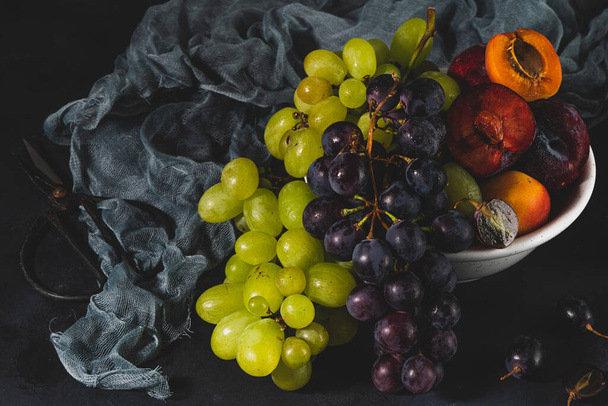 Frisch gewaschene Früchte mit Wassertropfen. Der helle High Key Look vermittelt Frische. Sorte von frischen Trauben, Aprikosen und Federn auf dunklem Hintergrund. Vitaminquellen aus Obst - Foto, Bild
