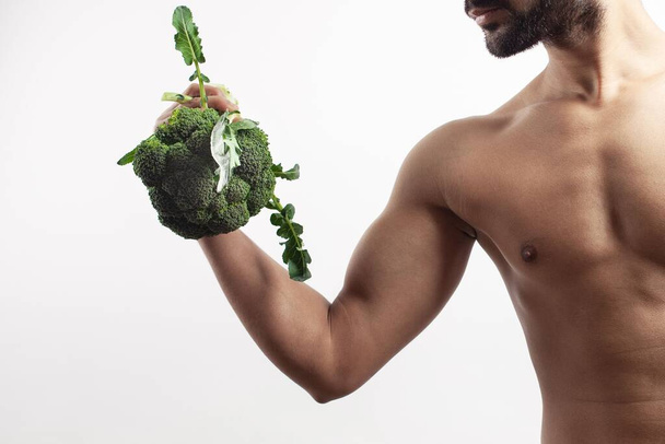 The concept of weigh loss and diet, a fit shirtless man sports posing with a broccoli in his hand - Foto, Imagen