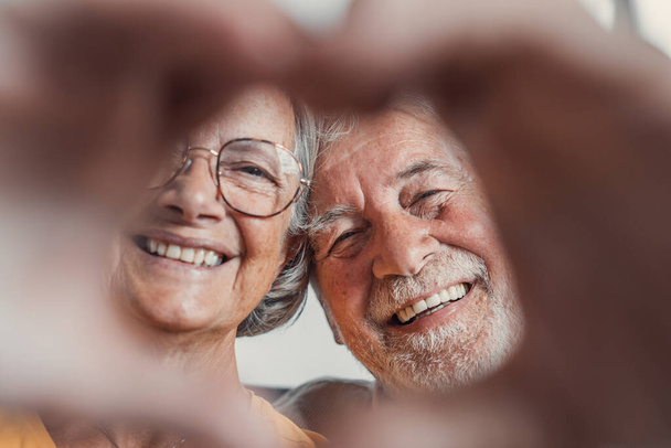 Close up portret szczęśliwy szczery w średnim wieku emerytowanych rodzin para robi gest serca palcami, pokazując miłość lub wykazując szczere uczucia razem w pomieszczeniach, patrząc przed kamerą. - Zdjęcie, obraz