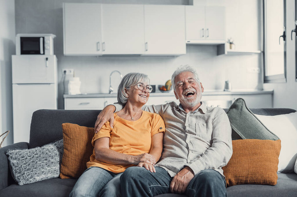 Happy mature husband and wife sit rest on couch at home hugging and cuddling, show care affection, smiling senior loving couple relax on sofa have fun, enjoy tender romantic family weekend together - 写真・画像