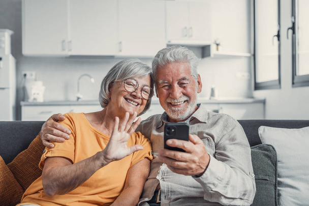 Счастливая семейная пара на пенсии пользуется мобильным телефоном для видеозвонков вместе, разговаривает с родственниками, получает хорошие новости, веселится, улыбается и смеется. Беззаботные взрослые пенсионеры общаются онлайн по мобильному телефону - Фото, изображение