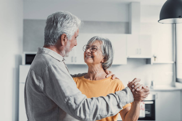Joyful active old retired romantic couple dancing laughing in living room, happy middle aged wife and elder husband having fun at home, smiling senior family grandparents relaxing bonding together - Foto, imagen