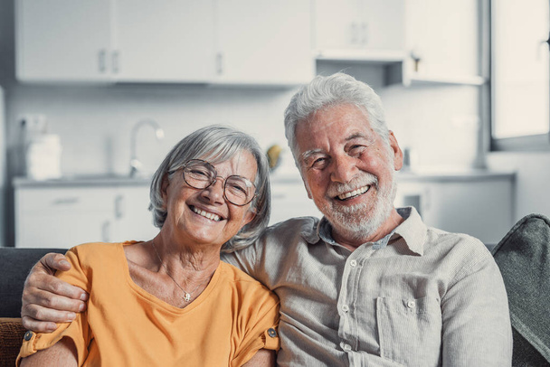 Kopfballporträt lächelnder älterer 60iger Jahre Mann und Frau sitzen entspannt auf dem Sofa und kuscheln, glückliches älteres Paar ruht auf dem Sofa im Wohnzimmer und umarmt den Blick in die Kamera, um Liebe und Fürsorge zu zeigen - Foto, Bild