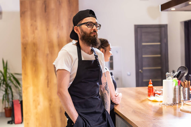 Χαρούμενος νεαρός σερβιτόρος επιχειρηματίας κοιτάζοντας τη φωτογραφική μηχανή, χαμογελαστή αρσενικό μικρό καφενείο επιχείρηση κάτοχος εργαζόμενος στέκεται στο εστιατόριο, χιλιαία επιχειρηματίας φορούν ποδιά που ποζάρει στο πορτρέτο καφετέρια - Φωτογραφία, εικόνα