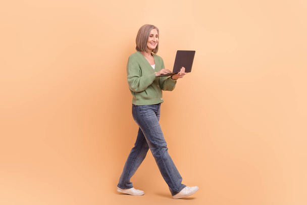 Full body cadre of walking professional senior businesswoman hold laptop online seminar teacher isolated on beige color background. - Foto, Bild