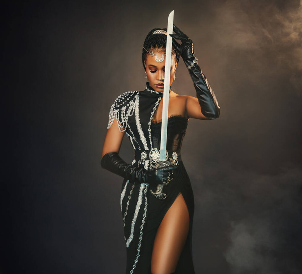 Portrait fantasy african american woman warrior holding sword weapon in hand. Dark queen girl in black military dress costume. Gothic lady elf fairy. Sexy beauty face fashion model pray. Studio photo. - Foto, immagini