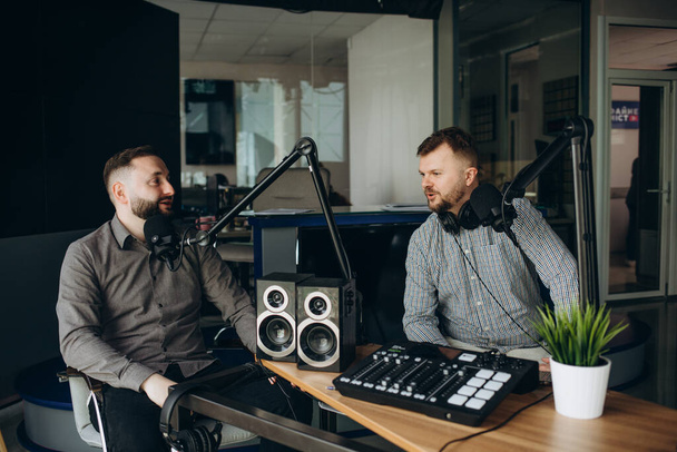 two smiling radio hosts talking while recording podcast in broadcasting studio. - Φωτογραφία, εικόνα