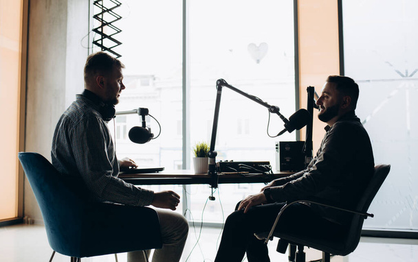 Two college podcasters laughing and having a good time in a studio. Two happy young men co-hosting a live audio broadcast. Two male content creators recording an internet podcast. - Photo, Image