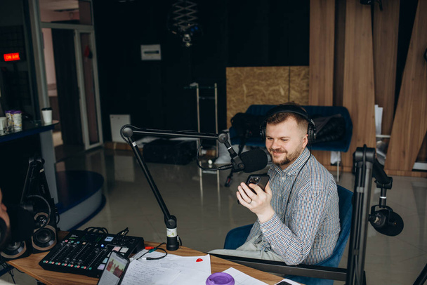 Portrait of young male radio host having a drink, looking focused while speaking in microphone, moderating a live show - Φωτογραφία, εικόνα