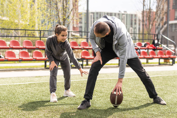 Schöner Papa mit seiner kleinen süßen Tochter hat Spaß und spielt American Football auf grünem Rasen. - Foto, Bild